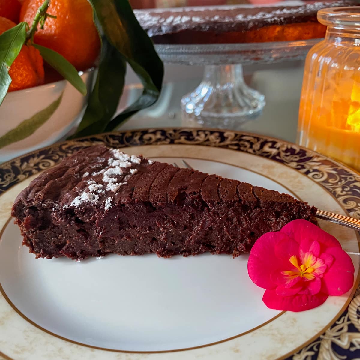 fondant slice of moist chocolate cake, topped with a little icing sugar next to a bowl of oranges