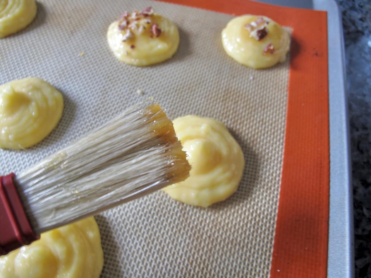 brushing egg yolk over choux pastry piped into mounds on a baking sheet