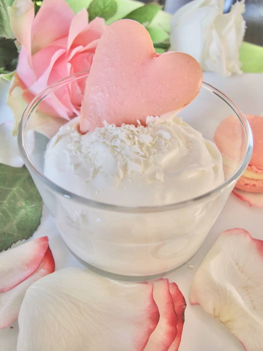 glass dish of white chocolate mousse garnished with chocolate shavings and a rose heart macaron shell