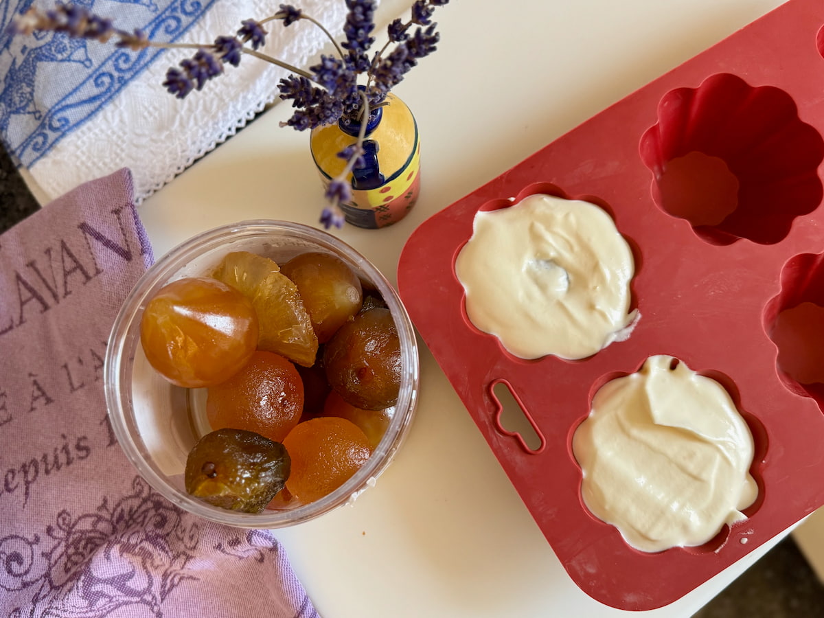 a tub of whole candied fruits next to silicone brioche moulds with ice cream made with whipping cream
