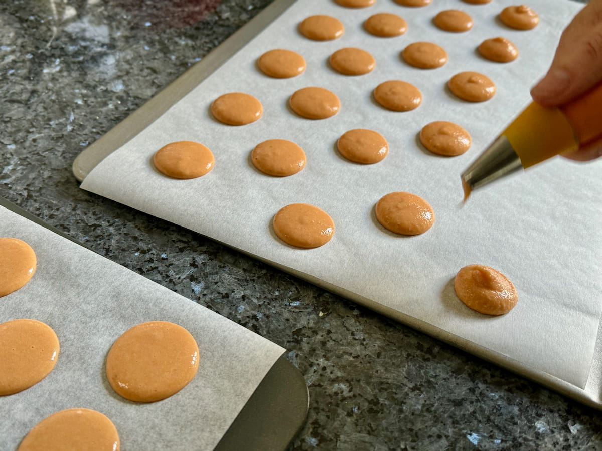 piping out little macaron rounds on a baking sheet