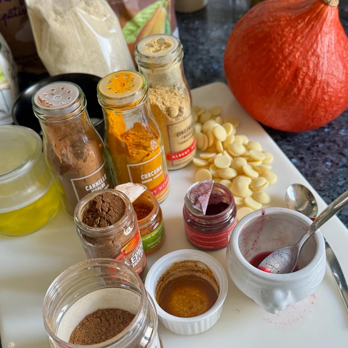 ground French spices in jars, along with powdered colourings, testing their colour appearance first in water next to a pumpkin