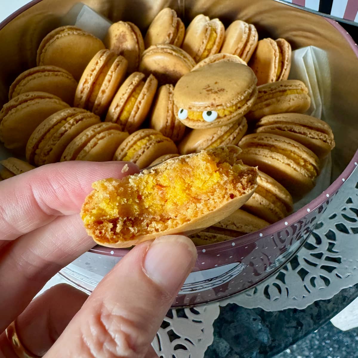 holding a half eaten pumpkin macaron showing its fondant ganache centre and crispy outside shell