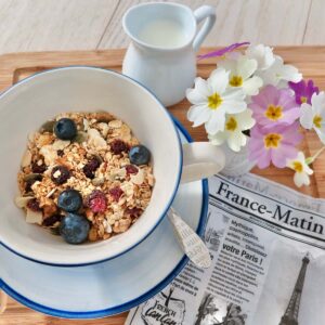 cup of homemade granola topped with fresh blueberries next to a French newspaper at breakfast