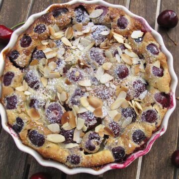 cherry clafoutis baked in dish topped with toasted almonds on rustic wooden table