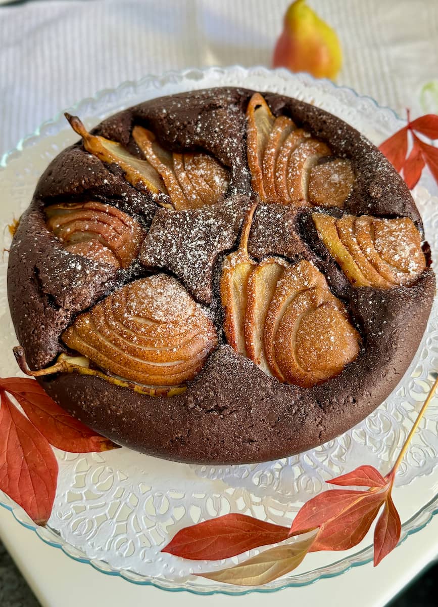 dark chocolate cake topped with sliced pear halves next to Autumn leaves