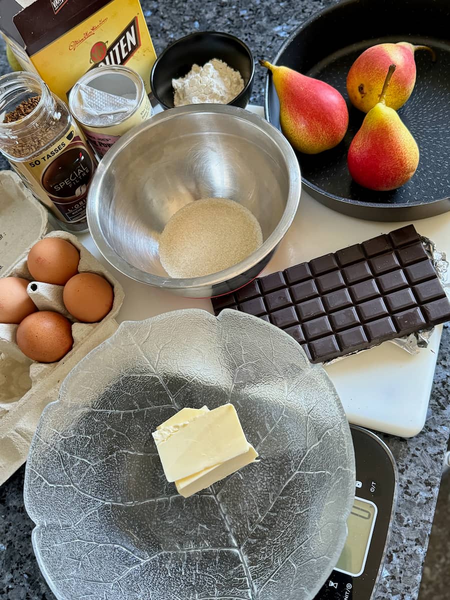 ingredients set out to make a chocolate cake with 3 pears - chocolate, eggs, sugar, butter, flour, baking powder and coffee
