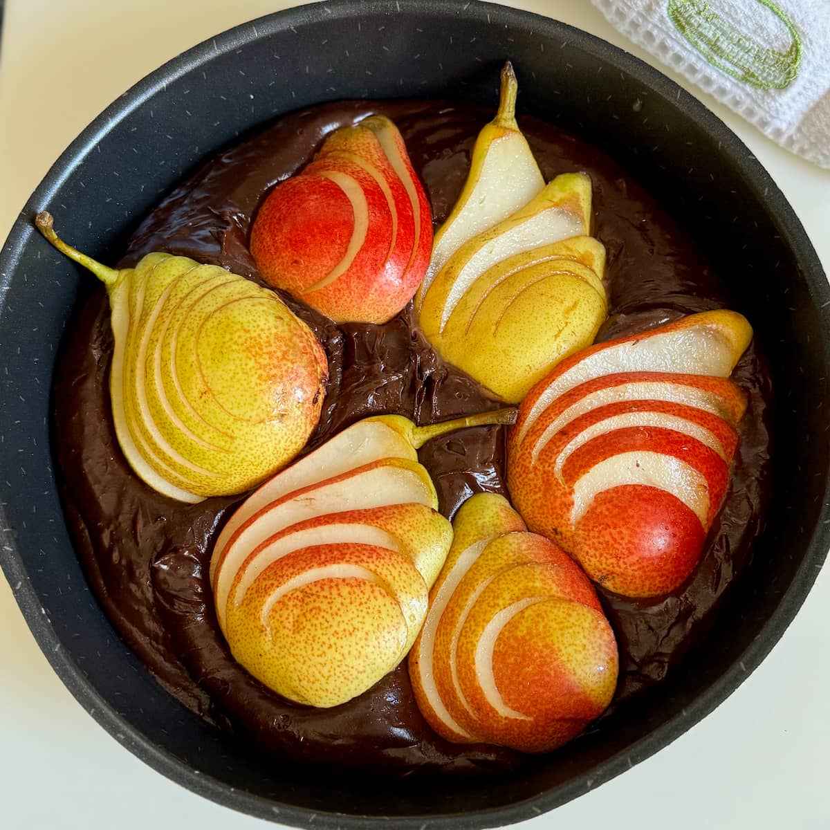 golden and russet fresh pear halves, sliced and topped on chocolate batter in a cake tin