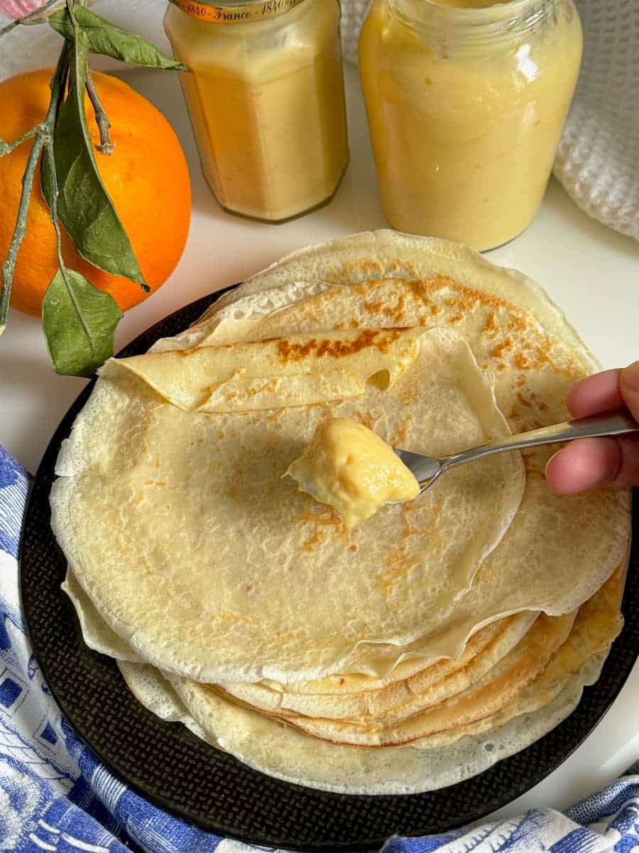 spooning orange curd on a pile of thin French pancakes