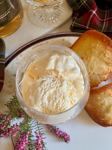 Whisky glass filled with soft scoop creamy ice cream next to almond cookies, heather and Whisky liqueur