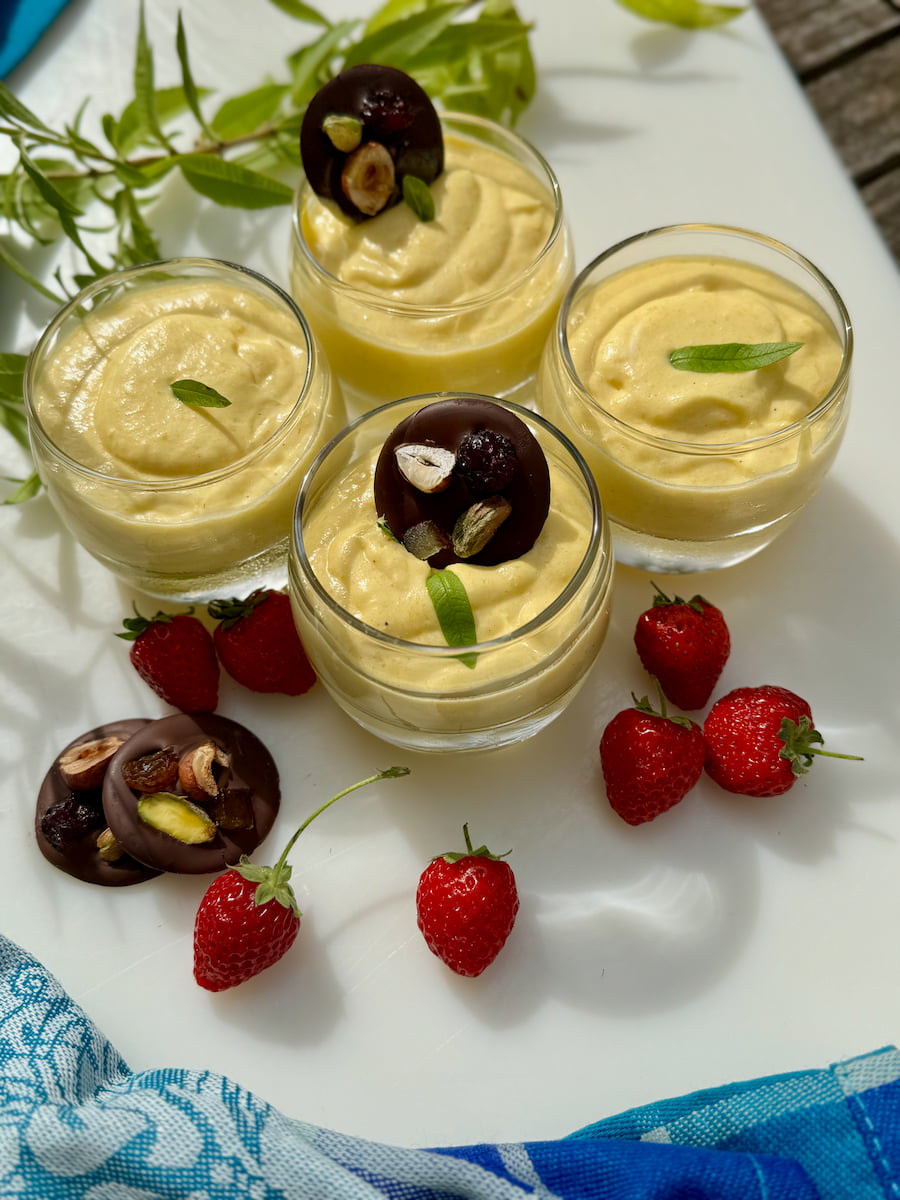 mini glass dishes with mango mousse topped with chocolate disks and surrounded by strawberries