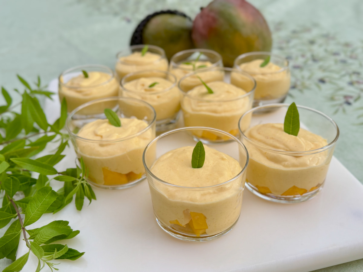 mango creams made with whipped cream and coconut milk on top of chopped fresh mango in glass dessert dishes 