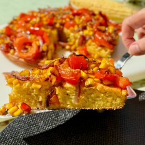 slice of cheesy cornbread topped with corn, bell pepper and red onion roasted on top
