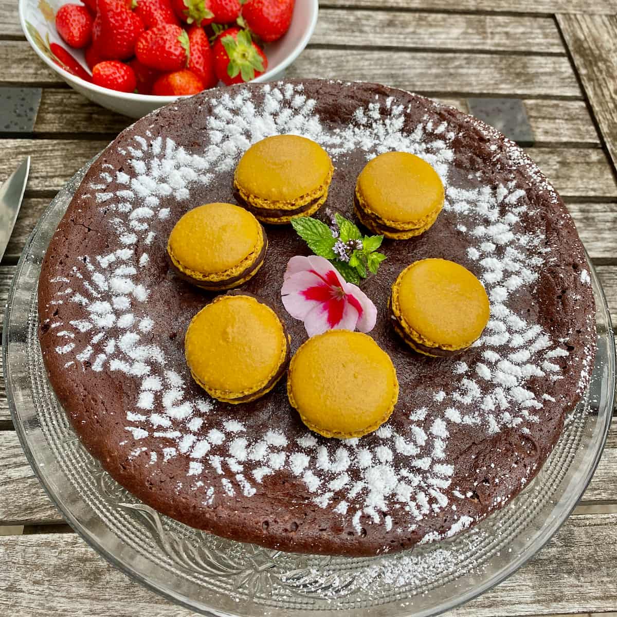 round one-layered chocolate fondant topped with pistachio macarons and decorated with icing sugar dusted over a doily