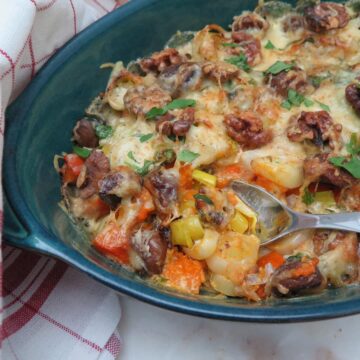 gratin dish with spoon taking out colourful butternut squash, toasted walnuts, chestnuts