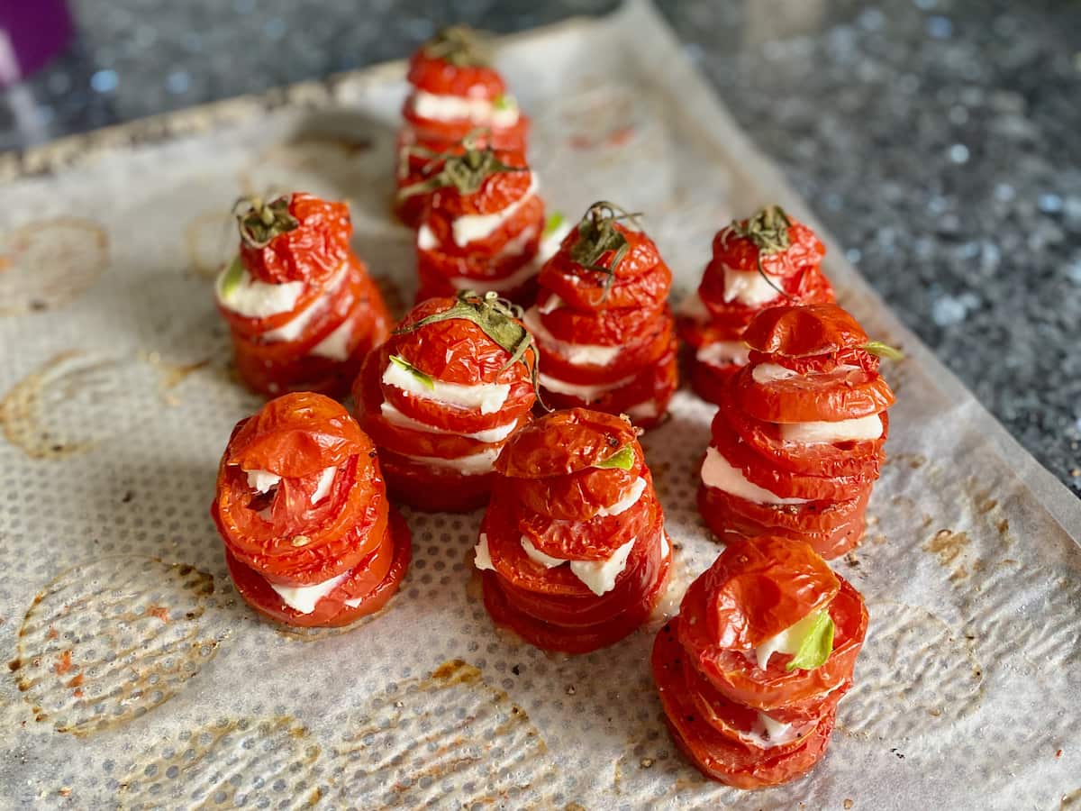 stacked roasted tomato slices on baking sheet with mozzarella slices