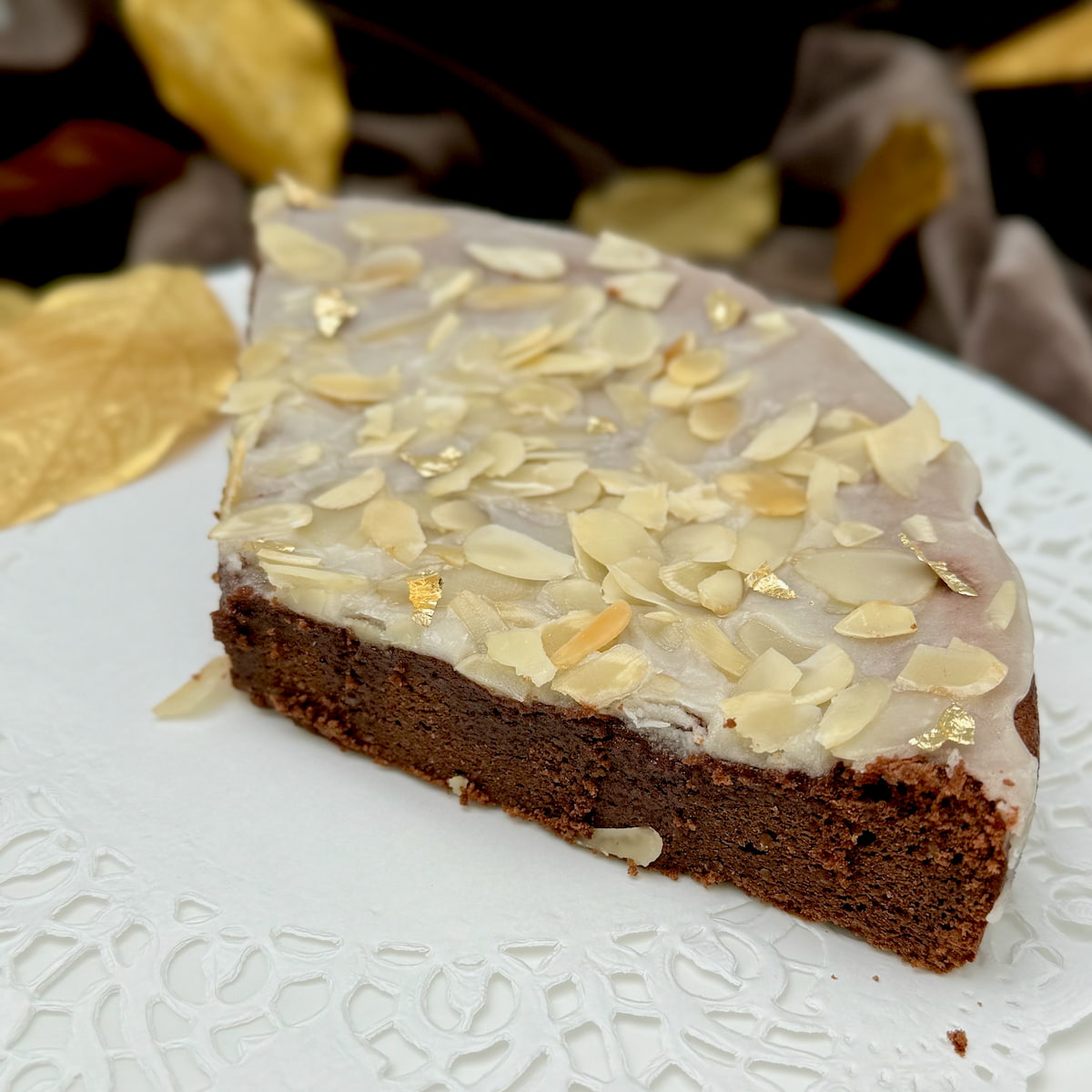 a large slice of chocolate cake topped with a rum glaze, toasted flaked almonds and gold leaf