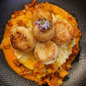 creamy risotto topped with seared scallops and chorizo sauce and an edible flower