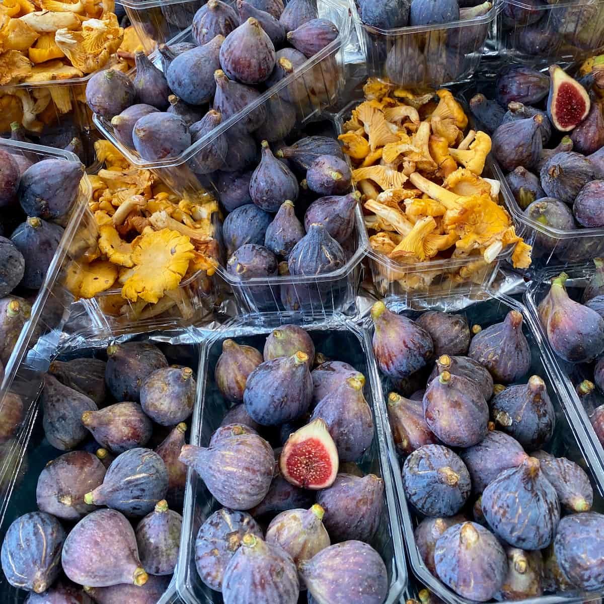 trays of purple fresh figs at the market next to girolle mushrooms