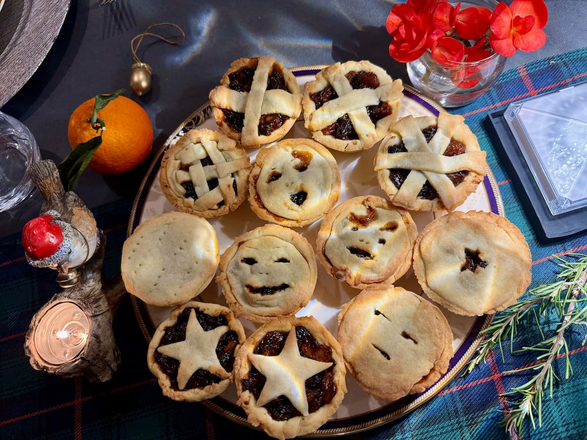 a plate of homemade mince pies with traditional pie toppings, stars but also spooky halloween type faces with mincemeat oozing out