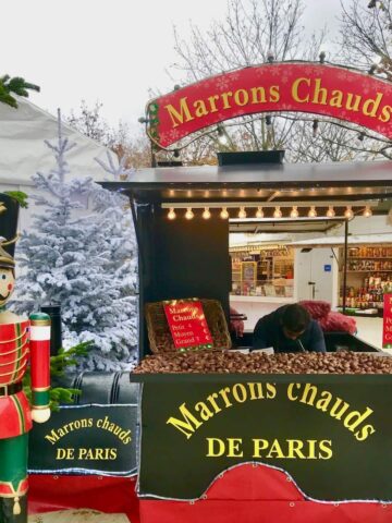 a stall selling roasted chestnuts at a French Christmas market with a sign saying Marrons Chauds next to a nutcracker.