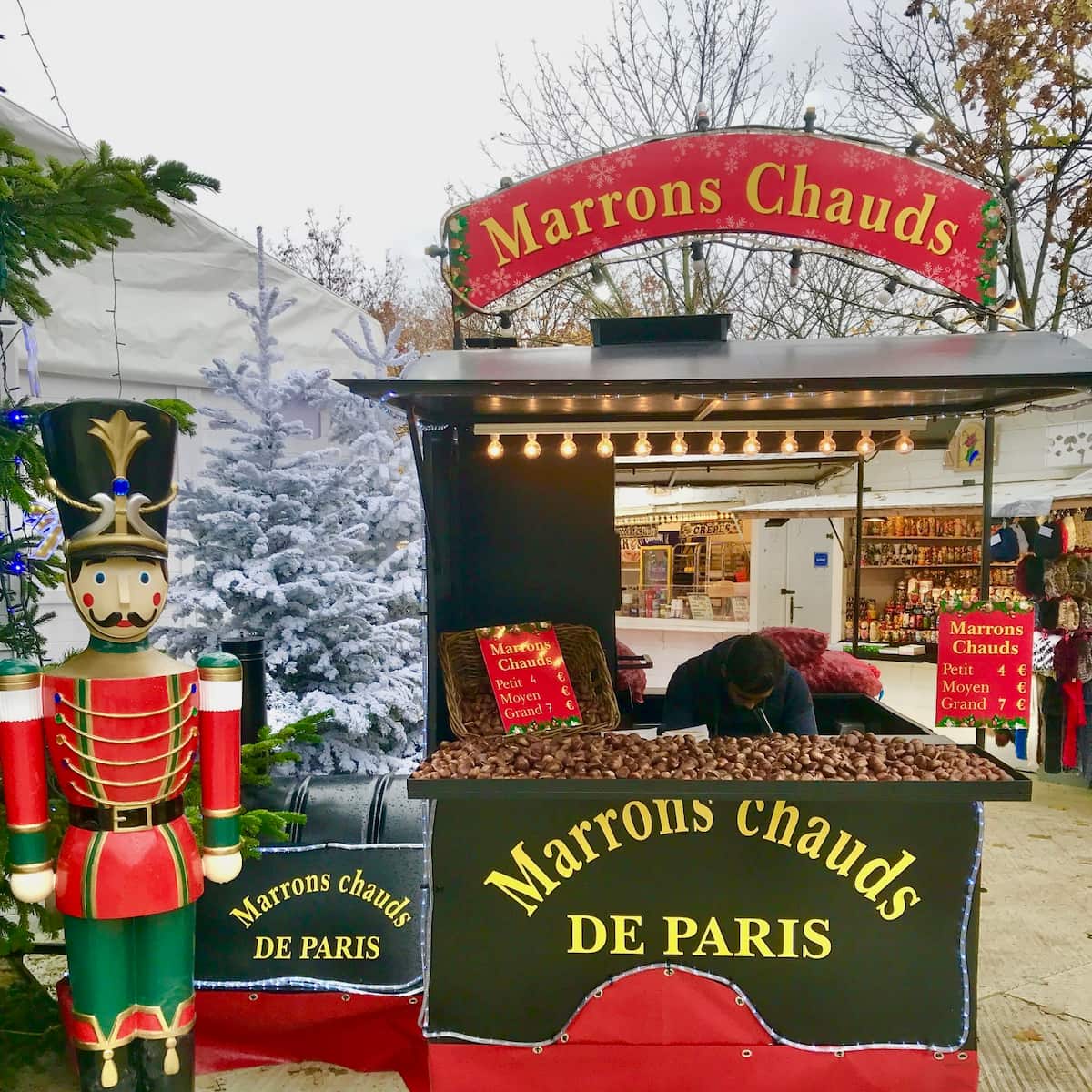 a stall selling roasted chestnuts at a French Christmas market with a sign saying Marrons Chauds next to a nutcracker.