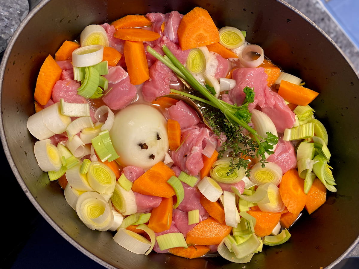 enamel pot with veal chunks, chopped leeks and carrots and fresh herbs plus an onion studded with 3 cloves