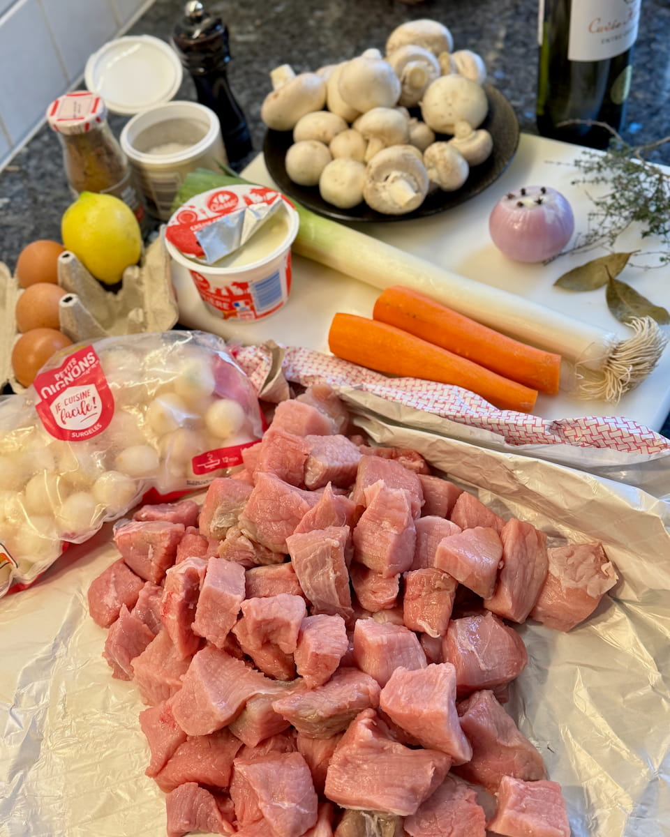 cubed veal laid out with other blanquette ingredients of mushrooms, carrots, lemon, egg yolks, a bouquet garni, crème fraîche, pearl onions and an onion studded with cloves.