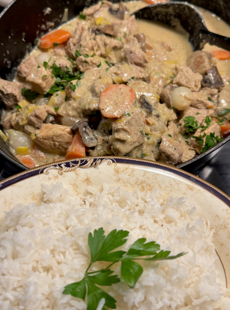 pot of French Blanquette veal stew with carrots, mushrooms and pearl onions next to a side dish of fluffy rice
