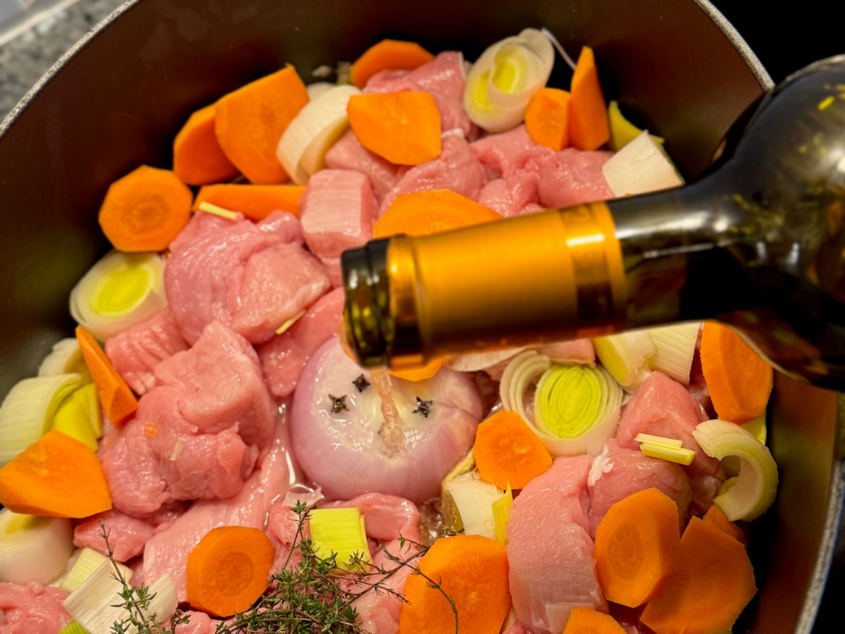 pouring white wine over veal chunks, carrots, leek and an onion studded with cloves