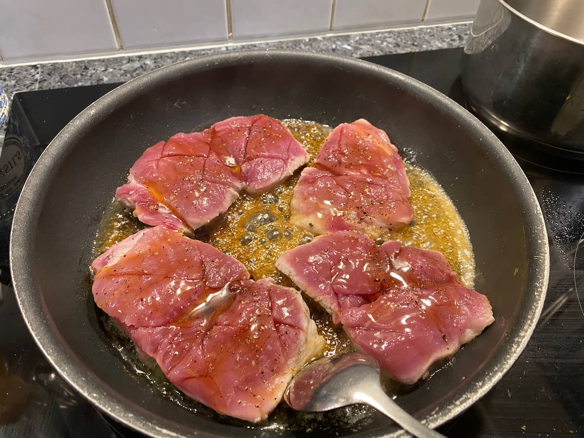 pork tenderloin cuts cooking in pan with bubbling honey