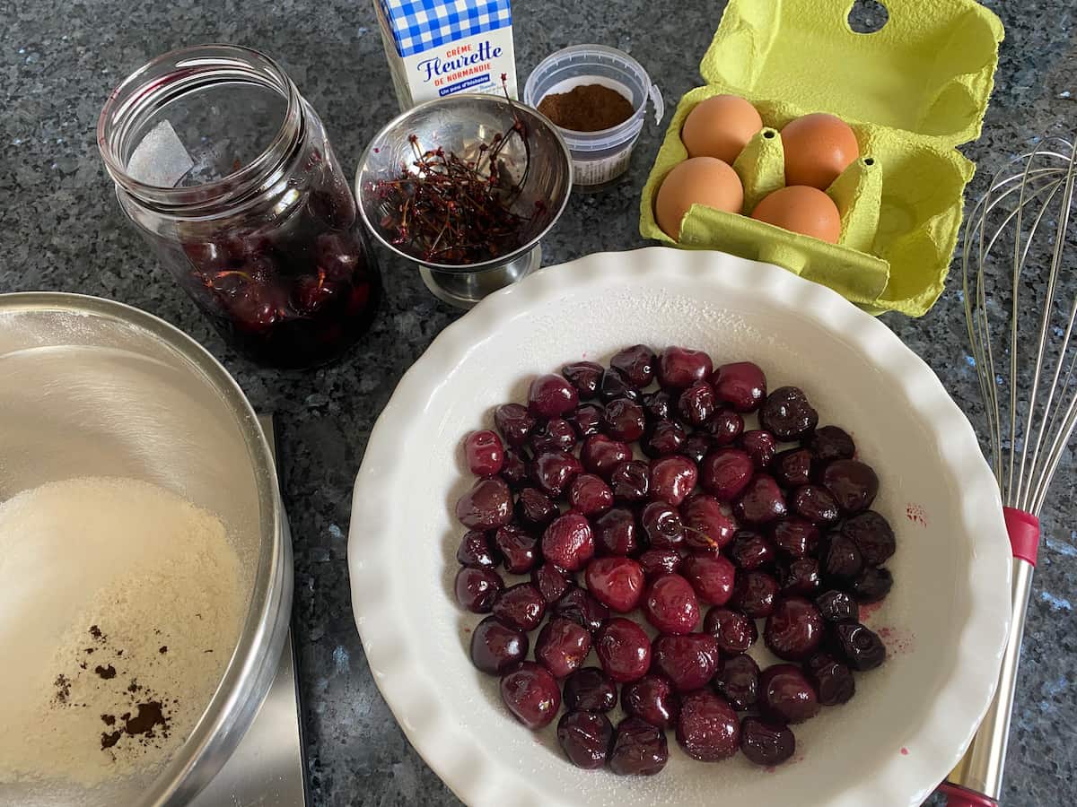 pie dish with roasted cherries surrounded by eggs and a cream batter and whisk
