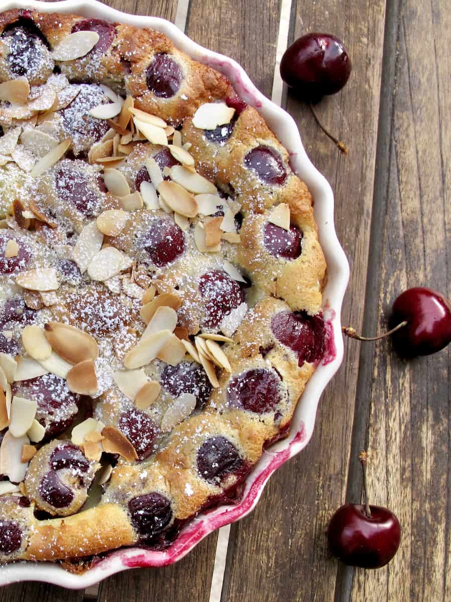 baked cherry custard in a pie dish sprinkled with powdered sugar and toasted almonds