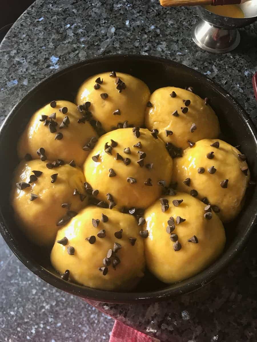 brioche buns in a cake tin covered in chocolate chips about to be baked