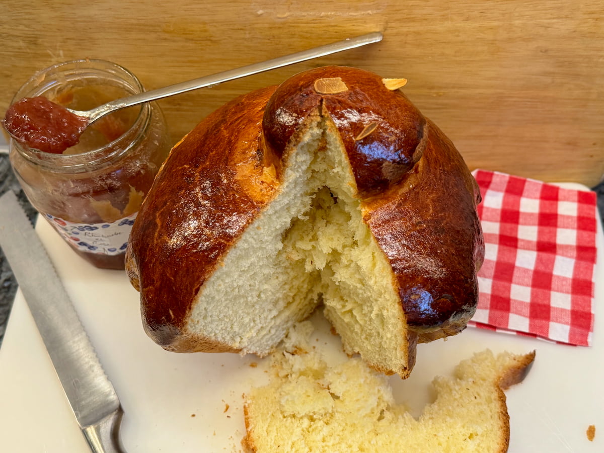 shiny glazed round brioche with a head cut through to reveal soft interior next to a pot of rhubarb jam