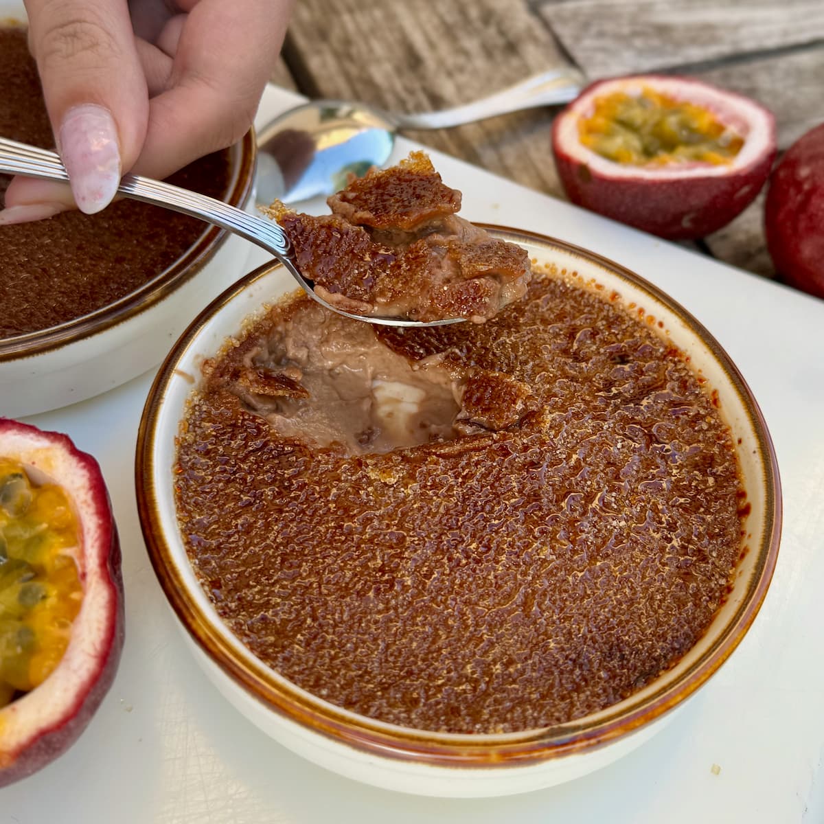 cracking in to a milk chocolate crème brûlée showing a delicious set custard topped with a thin caramelised crust - served with halved passionfruits