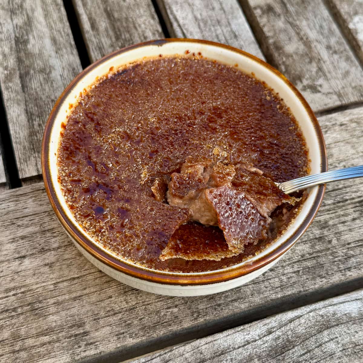 close-up of a chocolate creme brulee with spoon cracked through the caramel topping showing a milk chocolate custard underneath