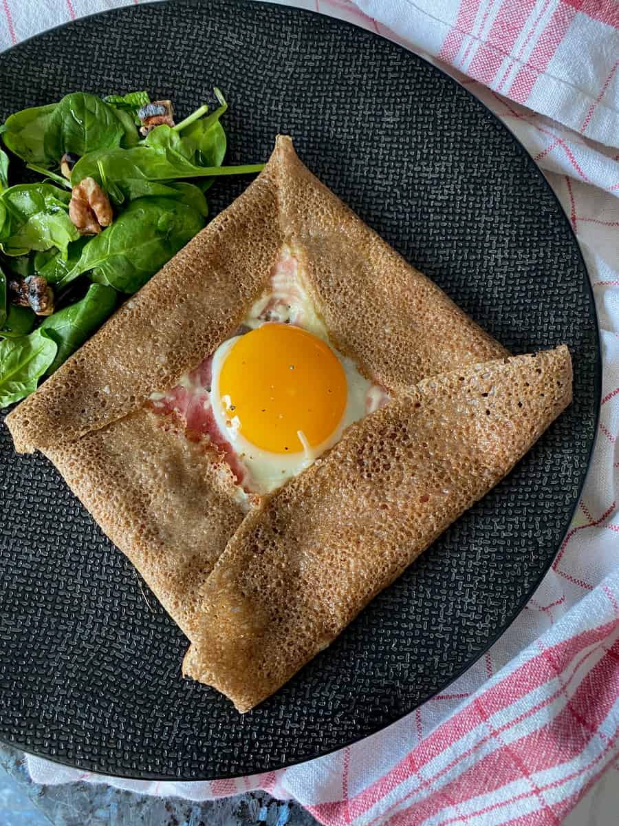 square brown pancake folded like an envelope with egg yolk in the middle surrounded with a little ham and cheese and side salad