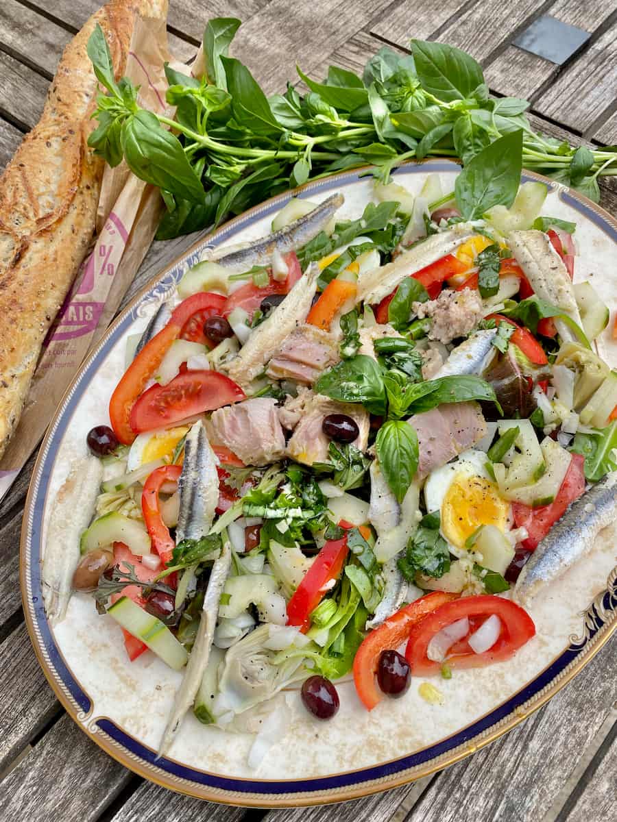large plate with a raw Nicoise salad of tuna, olives, tomatoes, basil and other fresh vegetables