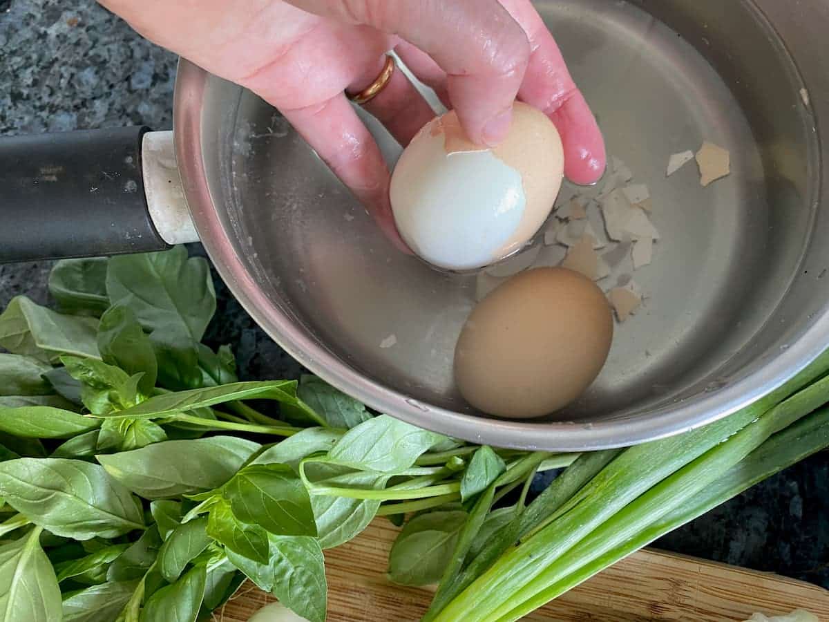 taking the shell off a hard boiled egg in a pan of water