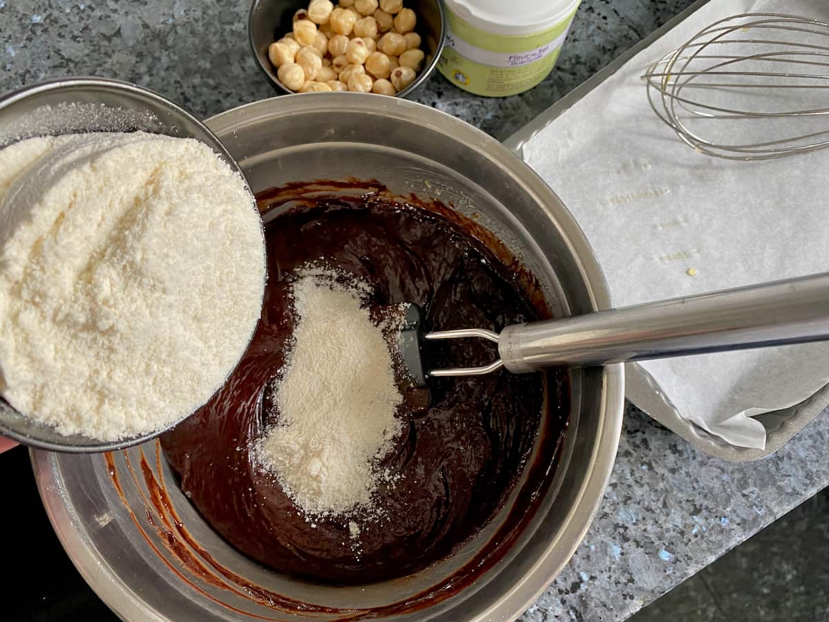 adding coconut flour to a bowl of chocolate brownie batter