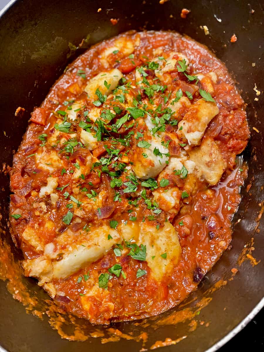cooking pot of a tomato fish stew topped with chopped fresh parsley