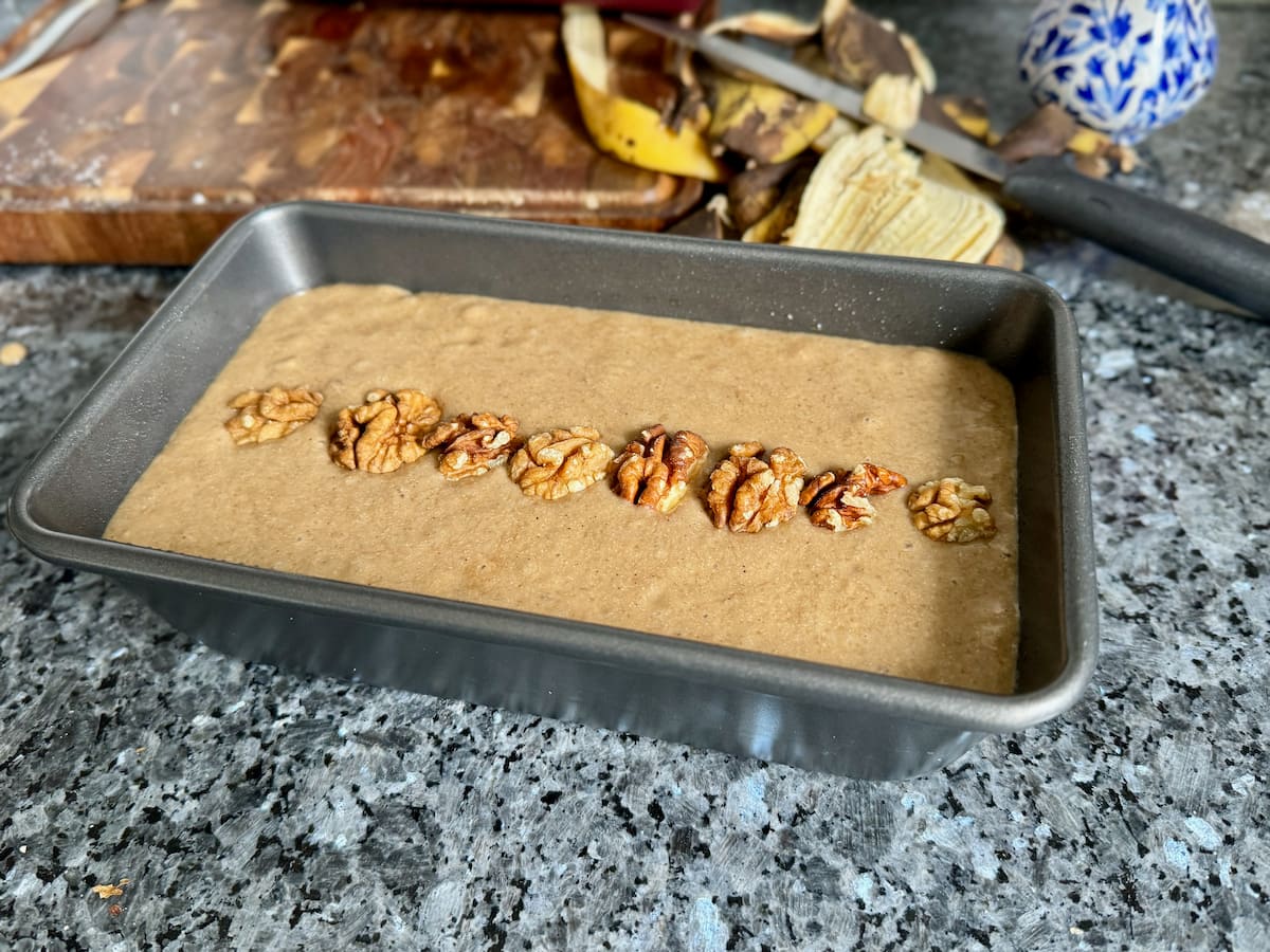 banana coffee cake batter in a 9x5 inch (900g) loaf tin topped with walnuts