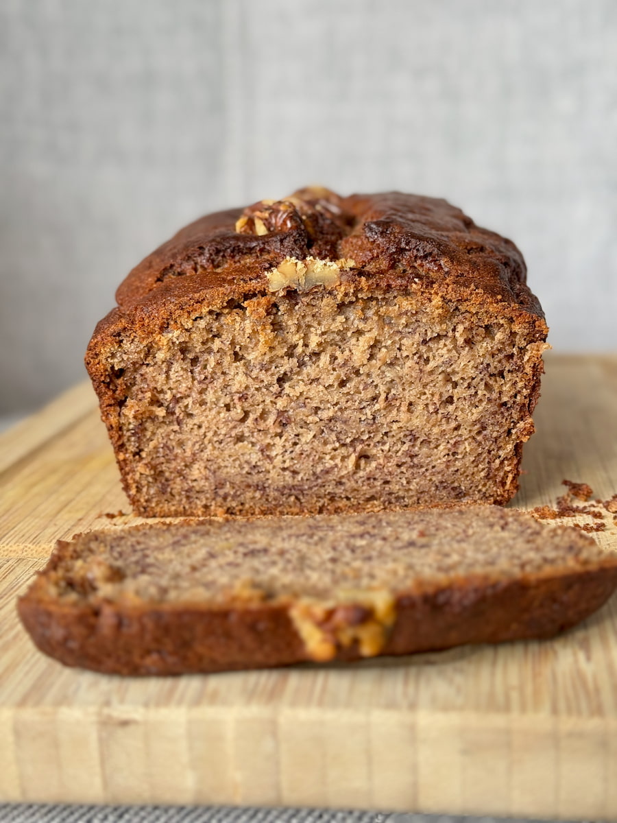 slice taken from a moist banana bread with coffee and topped with walnuts