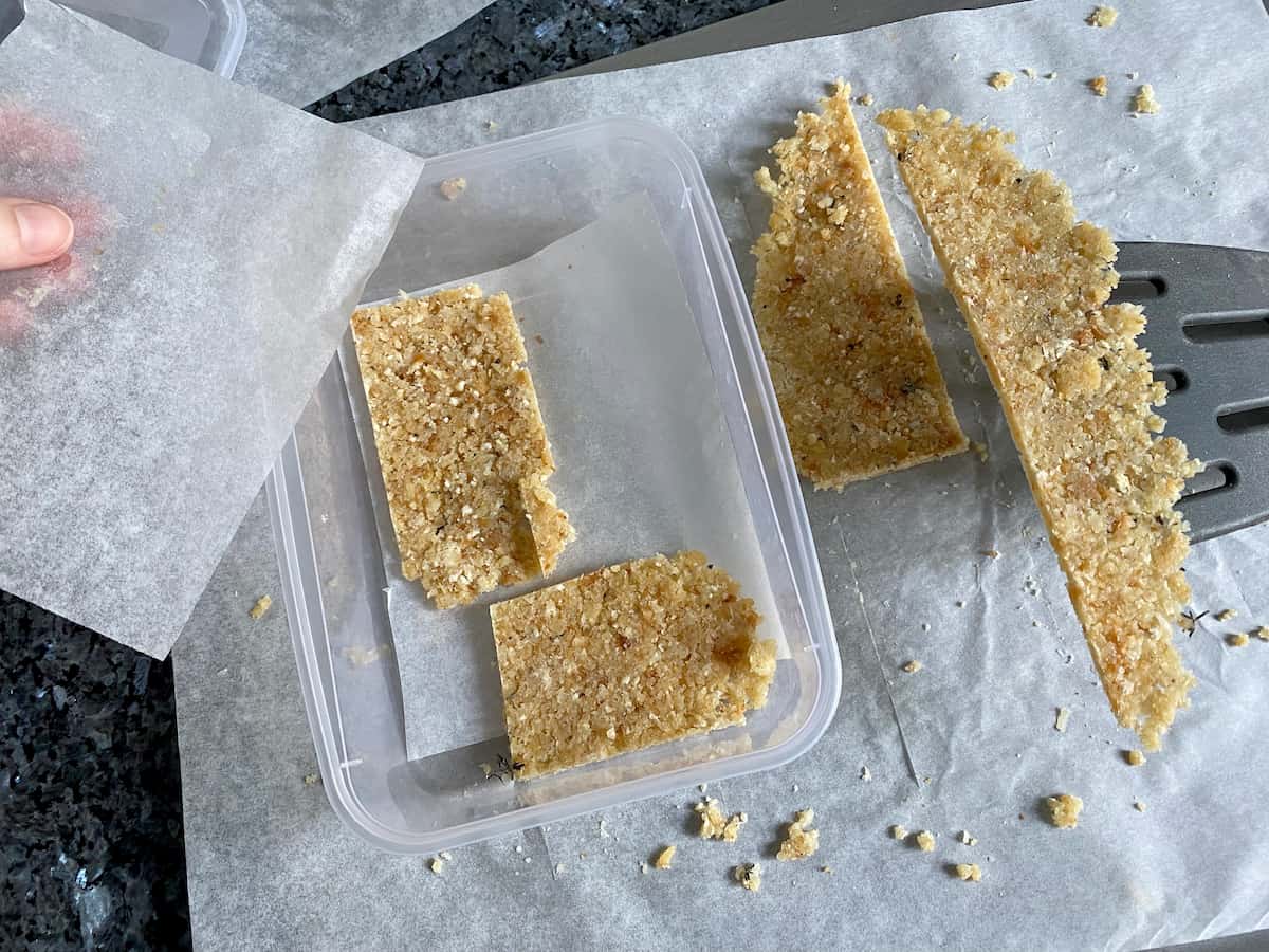 placing flat rectangles of herb crumble in a freezer-proof container separated with baking paper