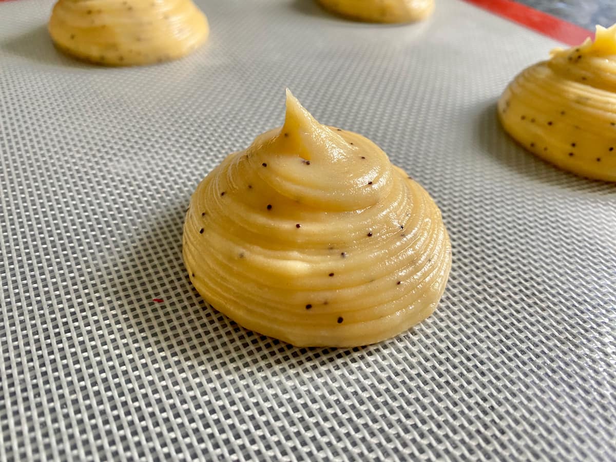savoury choux pastry dough with poppy seeds piped on a baking sheet