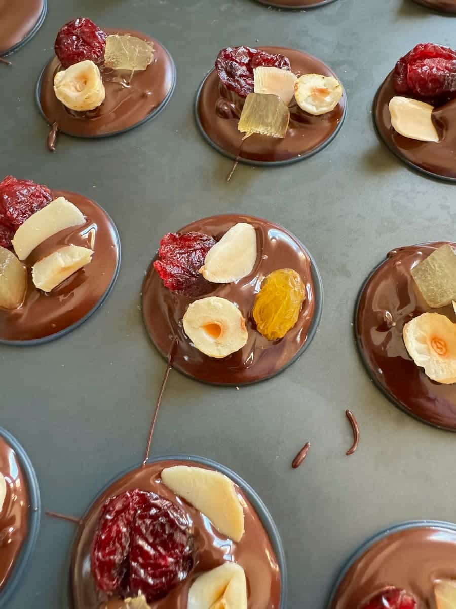 making mendiants of melted chocolate disks topped with dried fruits and nuts