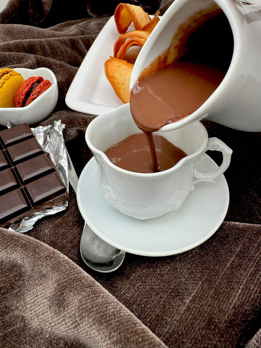 thick, dark hot chocolate being poured from a jug into a little porcelain cup
