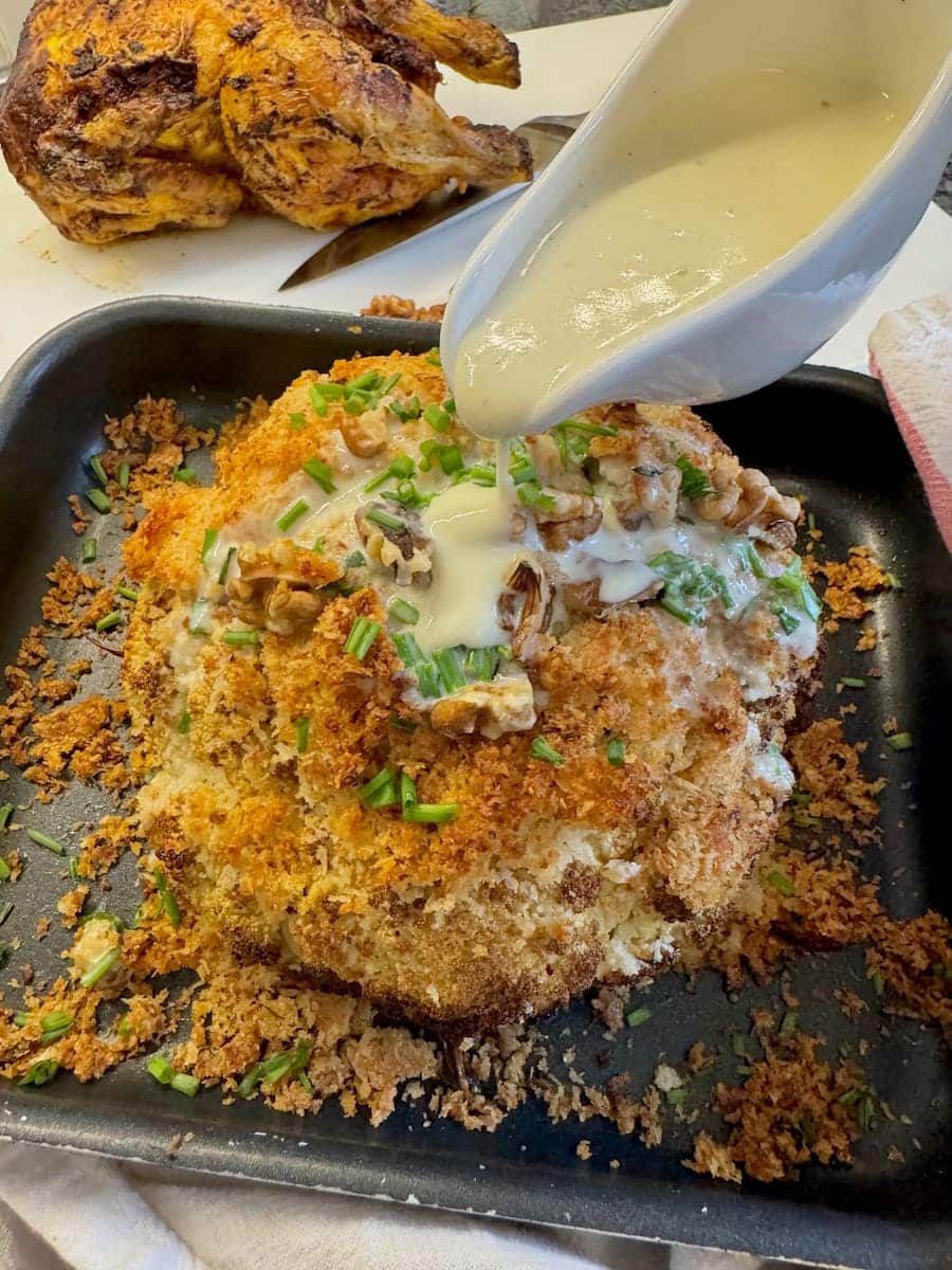 pouring white sauce over a roasted cauliflower cheese