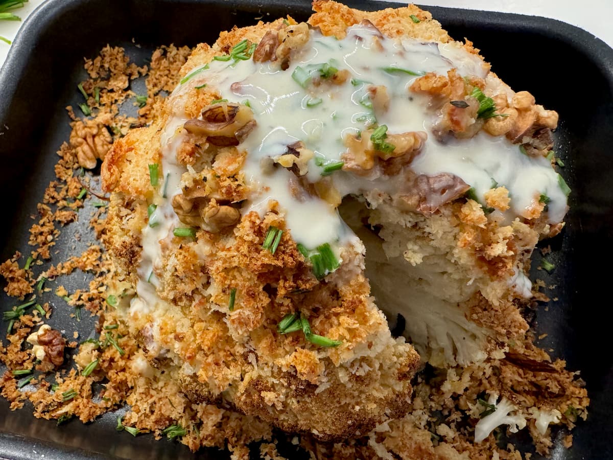 slice taken out of a whole roasted cauliflower with sauce, showing a crispy outside and tender inside